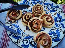 Apple roses made from puff pastry on a blue and white ceramic plate, artfully arranged with a knife on the edge of the plate.