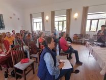 Participants sit in a bright room, listening attentively and quietly to a lecture.