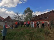 The workshop group is standing in front of a barn, listening attentively to a person explaining about seeds.