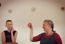 Two people, one thoughtfully placing their finger on their chin, while the other smiles and holds up an apple.