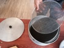 A person lifts a round sieve from a metal container, with a lid lying next to it on a table.